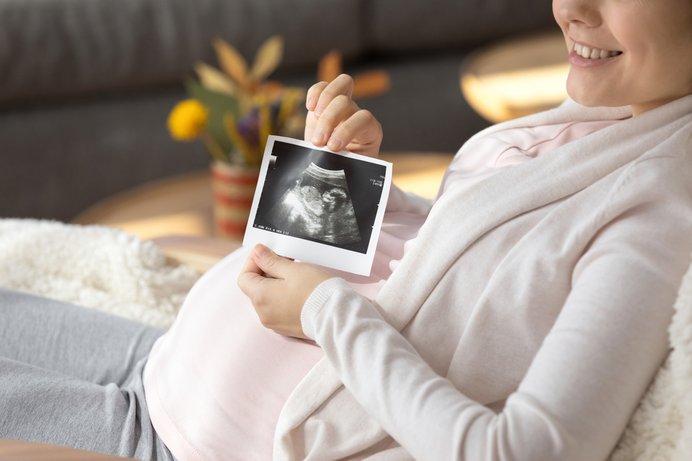 Crop,Close,Up,Of,Smiling,Young,Pregnant,Woman,Show,First